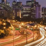 Have you been issued with a toll notice? multi lane warringah freeway in Sydney against zoomed in Bridge arch and skyscraper towers at sunset. Blurred lights of headlamps and stop signals of passing cars during rush hour in big city.