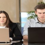 Apprehended Violence Orders Front view of two angry businesspeople using computers disputing at workplace and looking sideways each other with envy